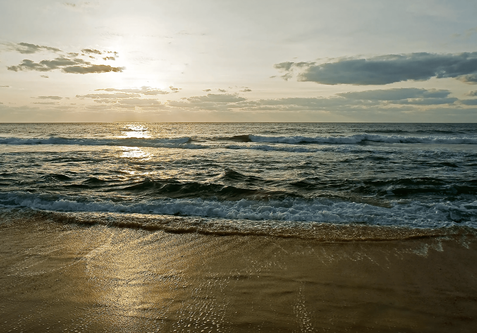 Sunset over the ocean with gentle waves.