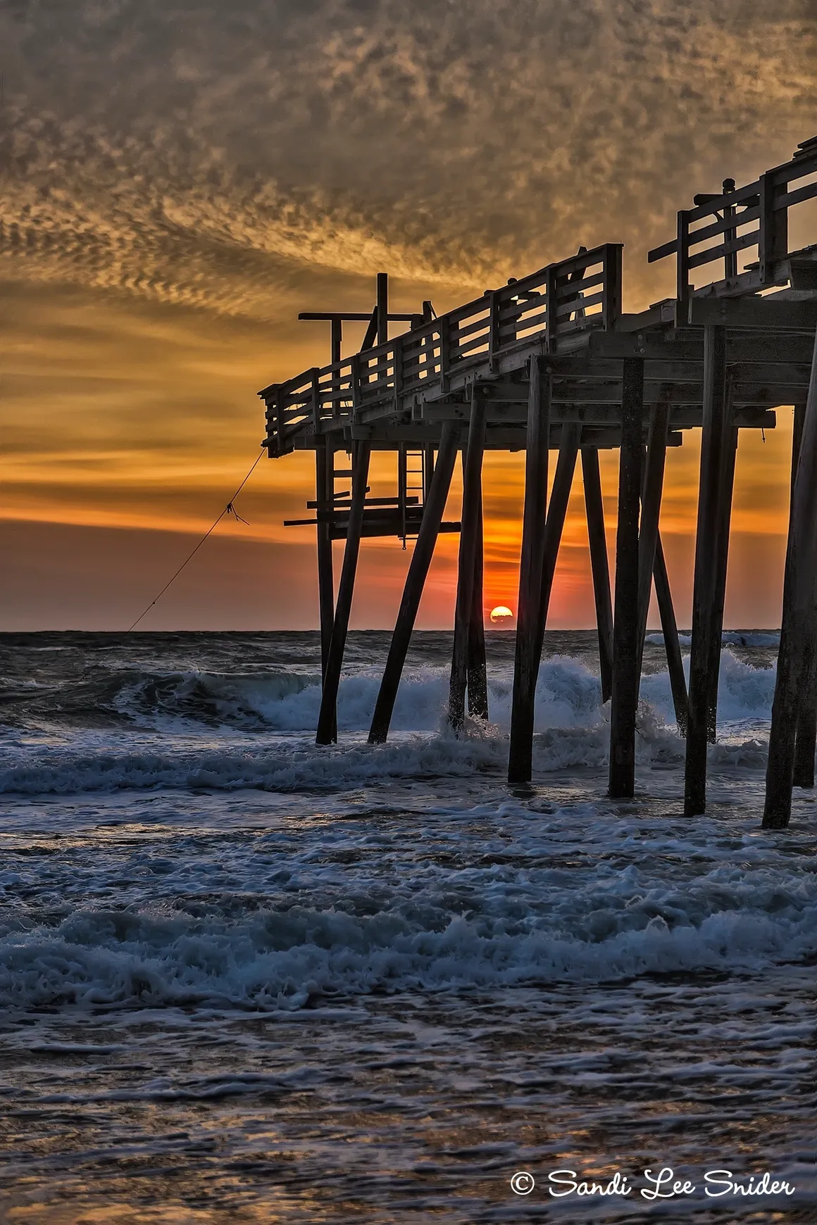 Sunset over ocean with wooden pier.