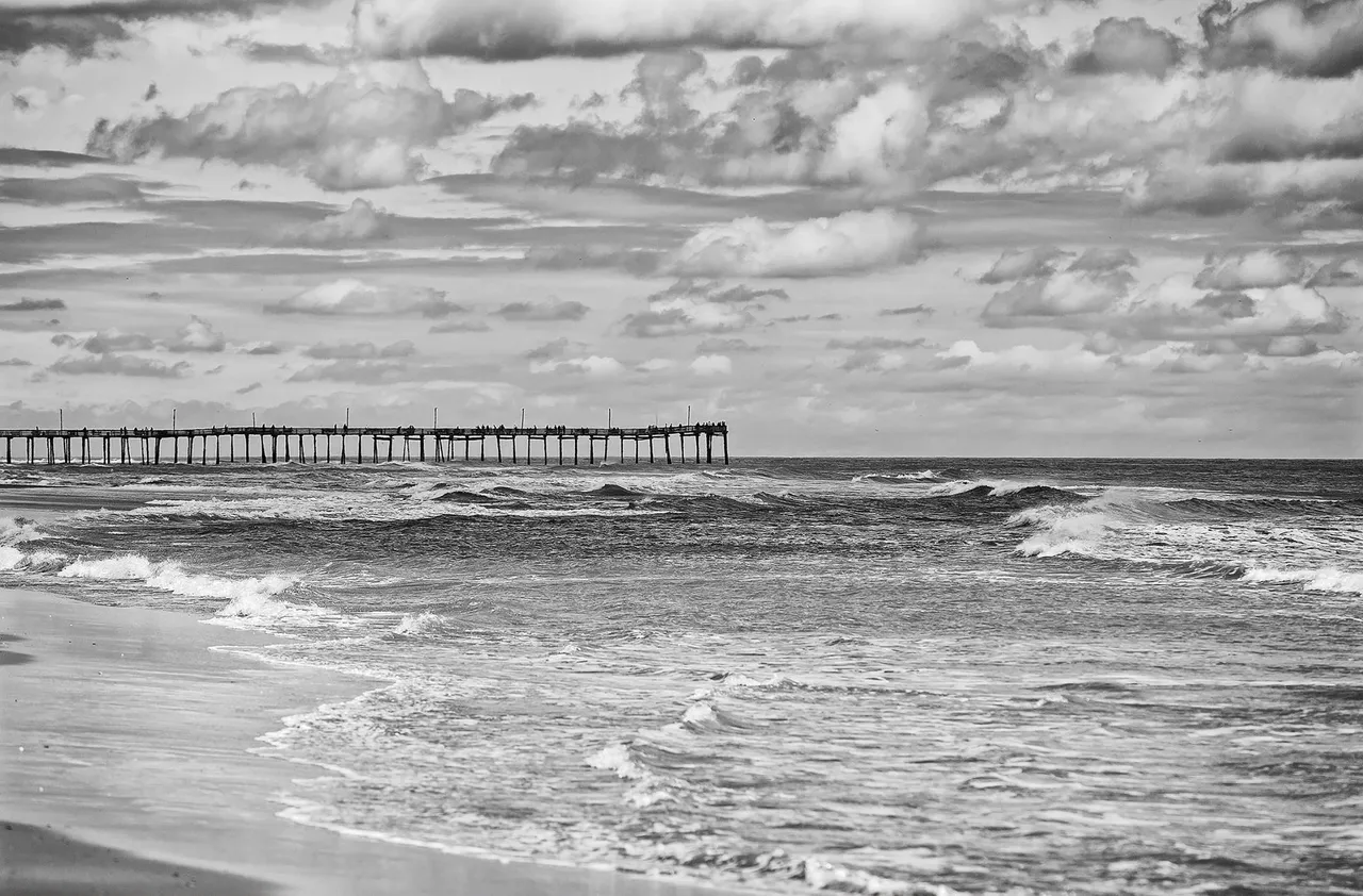 Black and white beach with pier view.