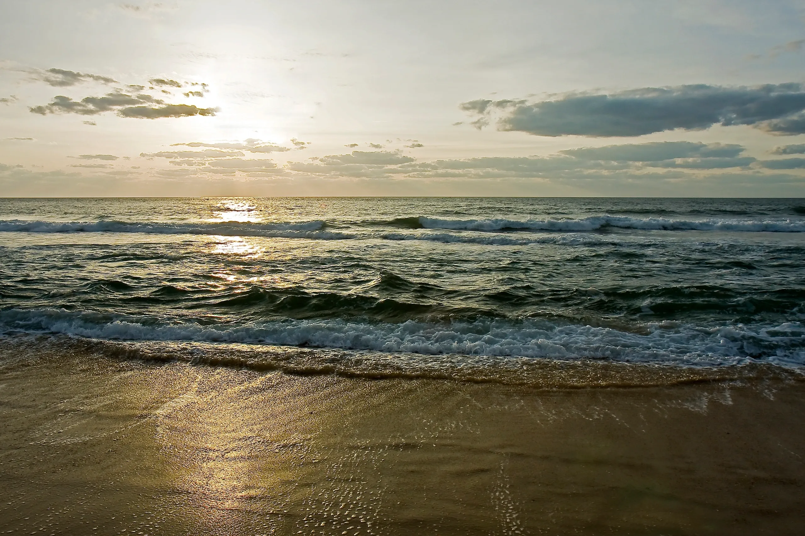 Sunset over calm ocean waves and beach.