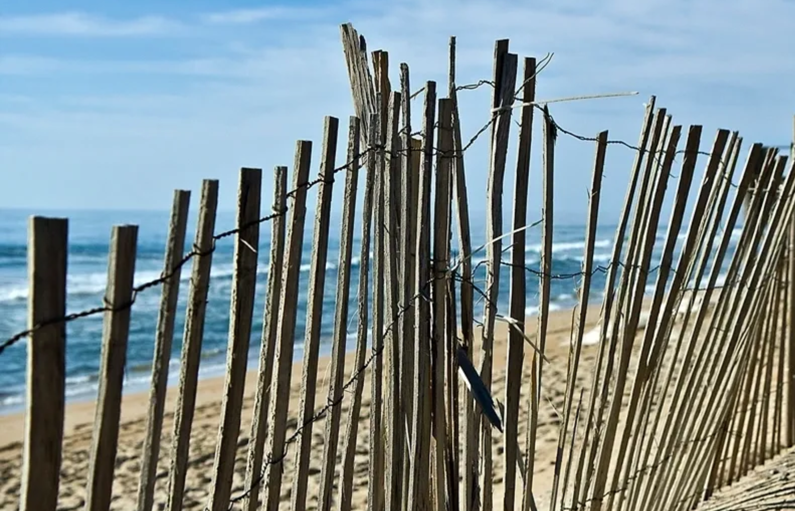 Weathered wooden fence on a sandy beach with ocean waves.