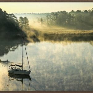 A sailboat anchored on a calm, foggy lake at dawn.